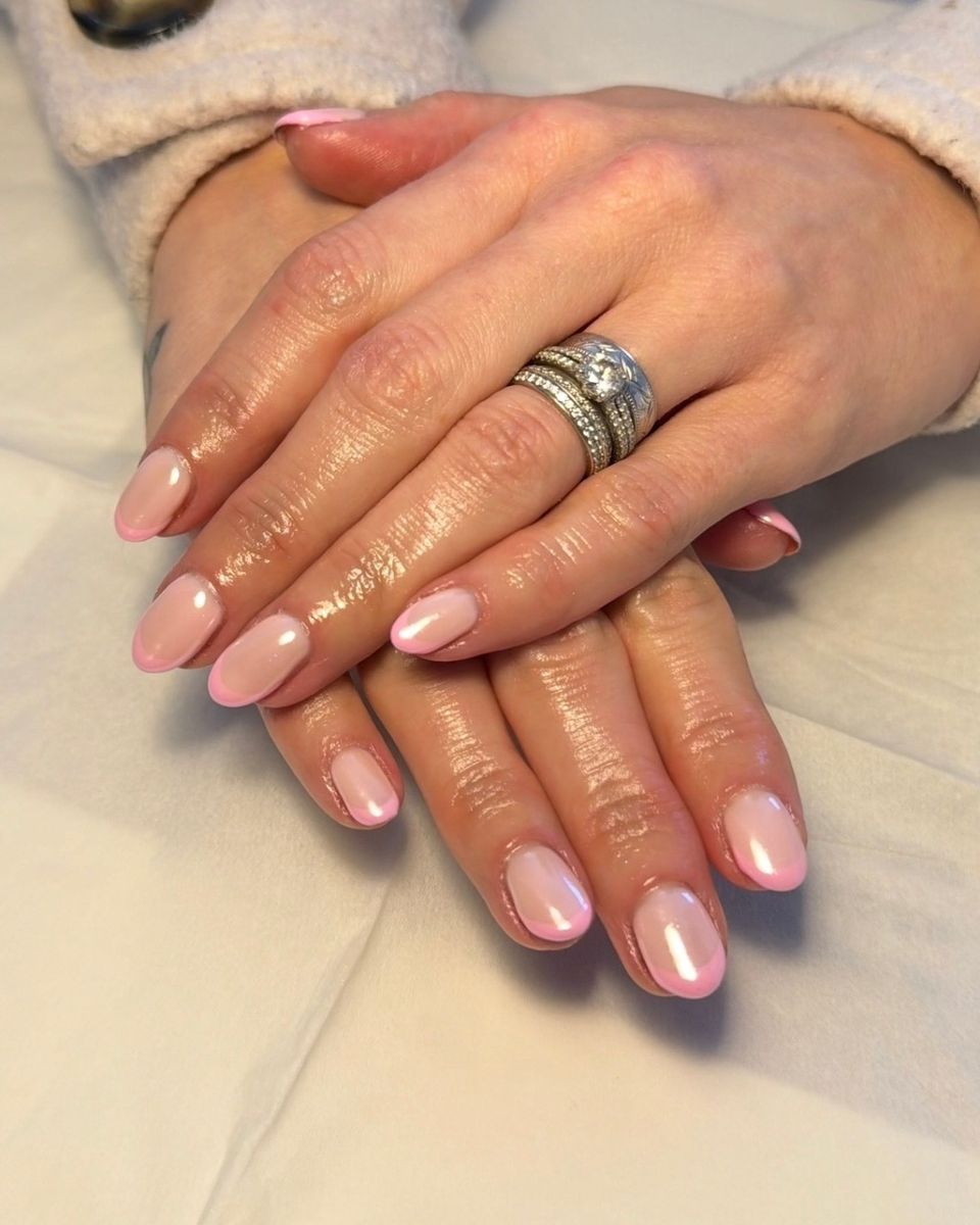 Soft pink French tip gel nails with a pearly chrome finish on a hand wearing rings